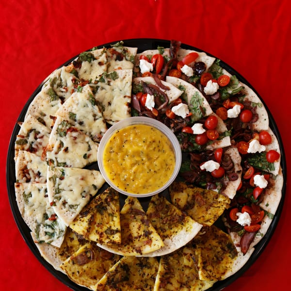A large platter of assorted Indian dosas, cut into triangles, with a central mango chutney dip.