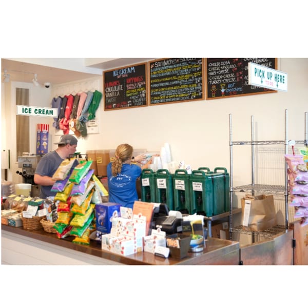 Two Hampton Chutney Co. employees working behind a counter with food, drinks, and menus.
