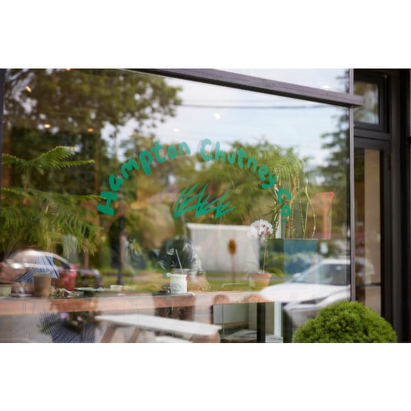 Hampton Chutney Co. logo on a glass window, reflecting trees and a white car outside.