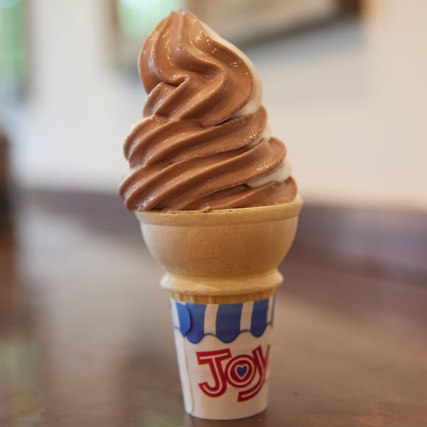 Swirled chocolate and vanilla soft-serve ice cream in a waffle cone with a 'Joy' wrapper.