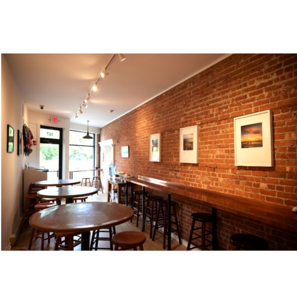 Interior of Hampton Chutney Co. with brick walls, wooden tables, bar seating, and framed artwork.