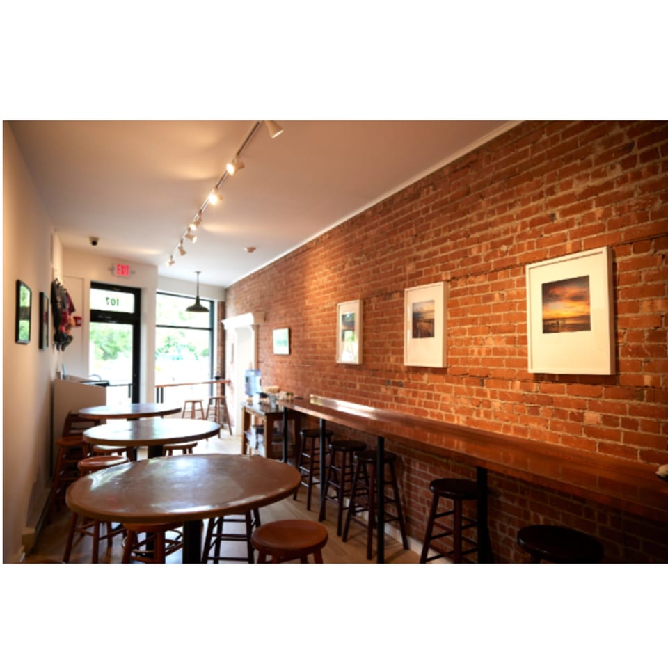 Interior of Hampton Chutney Co. with brick walls, wooden tables, bar seating, and framed artwork.