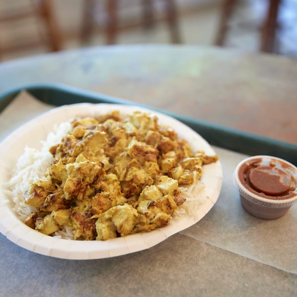 Indian chicken and rice dish with a side of chutney, served on a paper plate.