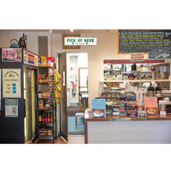 Interior view of Hampton Chutney Co. with a counter, menu board, and a chef in the background.