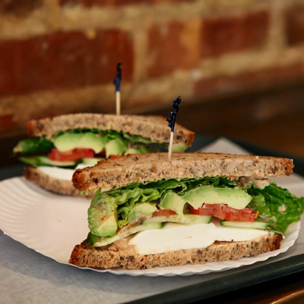 Two Hampton Chutney Co. sandwiches with avocado, tomato, cucumber, and cheese on whole wheat bread.