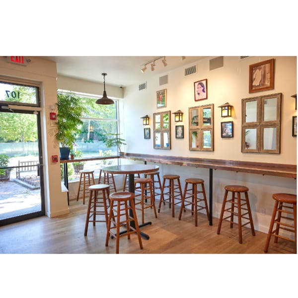 Interior of Hampton Chutney Co. with high tables, wooden stools, and framed art on the wall.