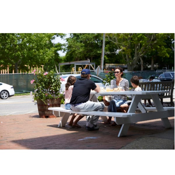Family of four enjoying a meal at an outdoor picnic table on a sunny day.