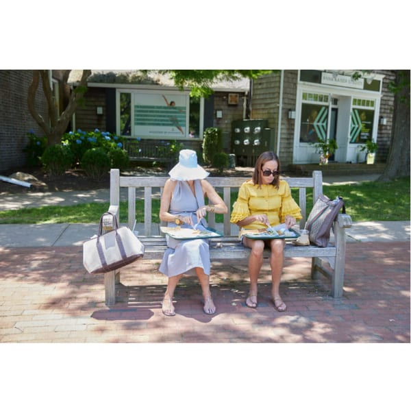 Two women eating Hampton Chutney Co. food on a park bench outside on a sunny day.