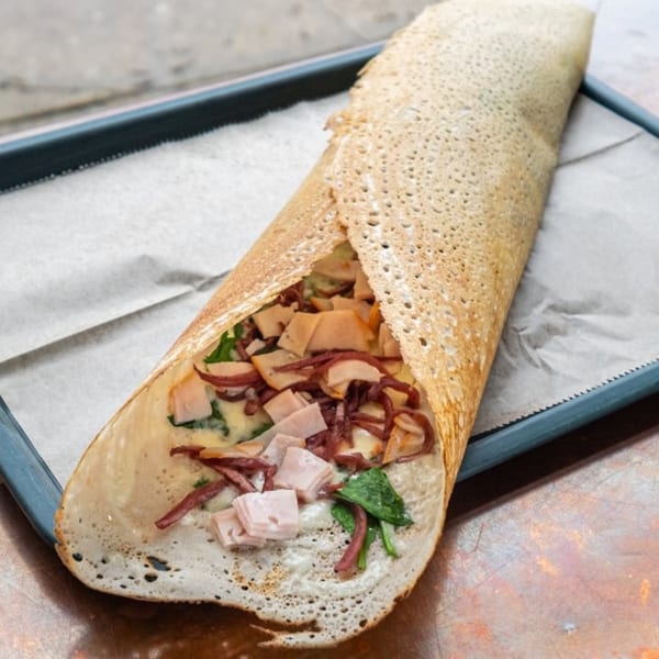 Savory crepe filled with ham, spinach, and cheese sauce on parchment paper in a blue tray.