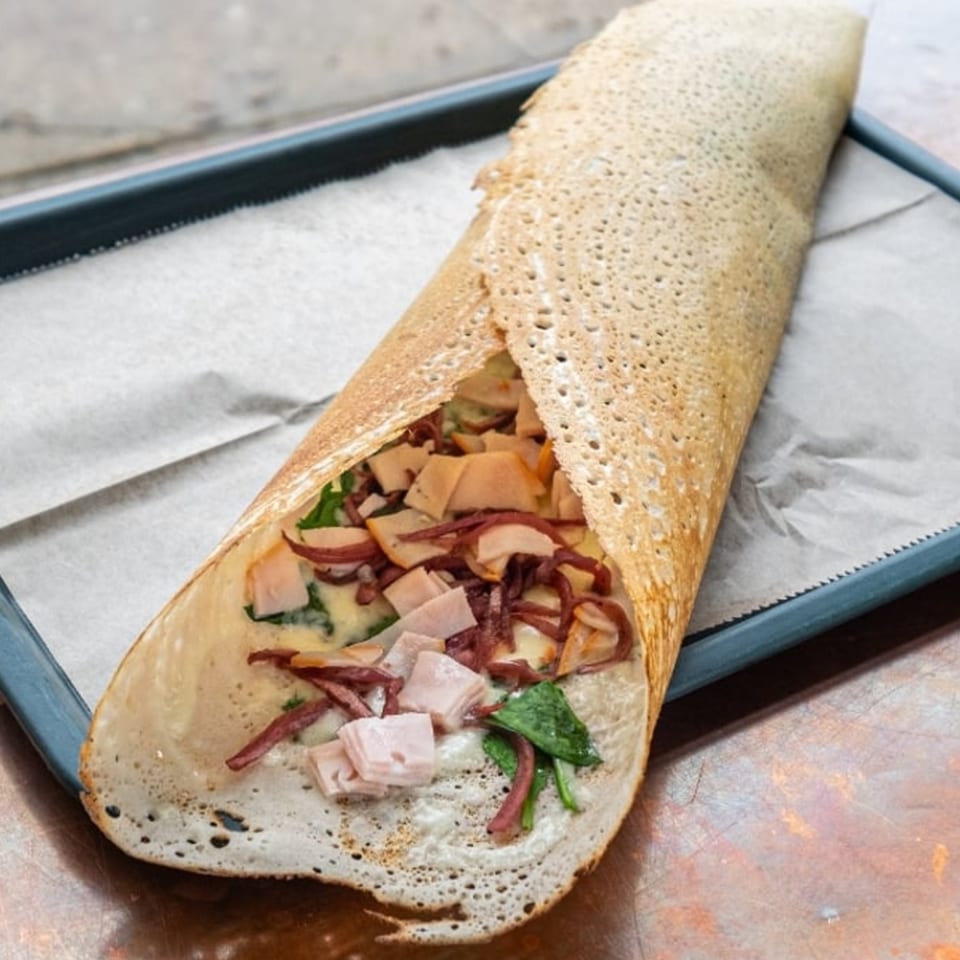 Savory crepe filled with ham, spinach, and cheese sauce on parchment paper in a blue tray.