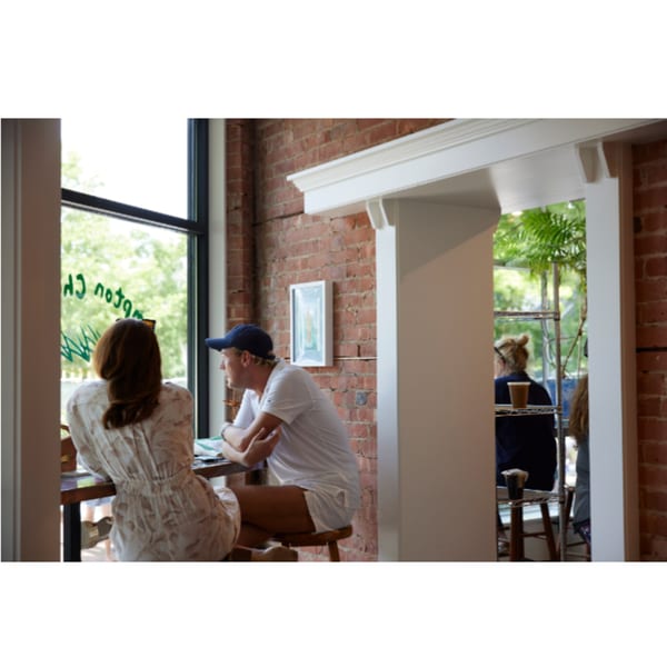 Two customers sit at a window counter in Hampton Chutney Co., with brick walls and greenery outside.