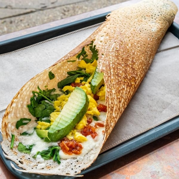 Savory crepe filled with scrambled eggs, spinach, avocado, and sun-dried tomatoes on a tray.