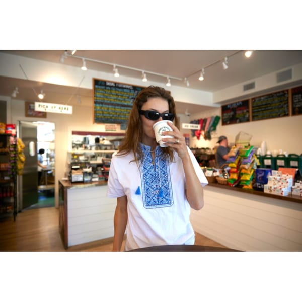 A woman in sunglasses sips from a coffee cup inside Hampton Chutney Co.
