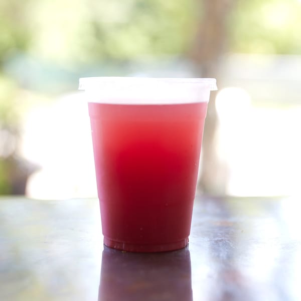 A vibrant red drink in a clear plastic cup with a lid, on a reflective surface.