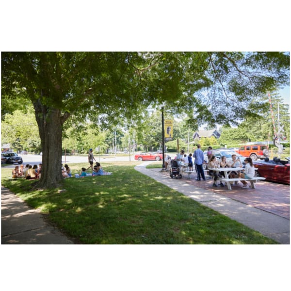 People enjoying outdoor seating at Hampton Chutney Co., some at picnic tables, others on the grass.