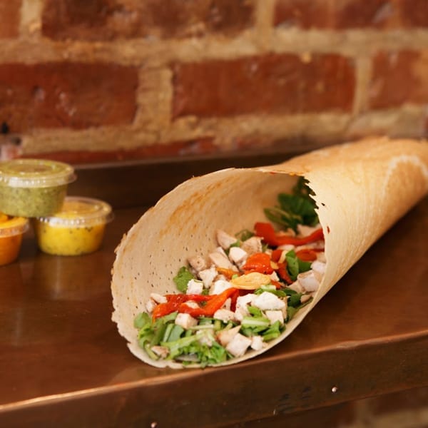 A Hampton Chutney Co. dosa filled with chicken, red peppers, and greens, with chutneys in the background.