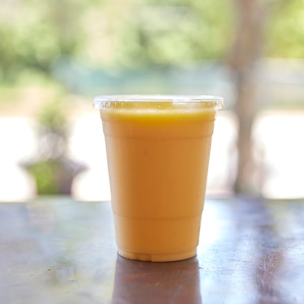 A Hampton Chutney Co. mango lassi in a plastic cup on a wooden table.