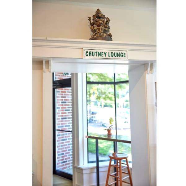 A Ganesha statue above a "CHUTNEY LOUNGE" sign, with a bar stool and window visible below.