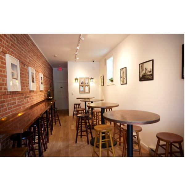 Interior of Hampton Chutney Co. with brick wall, bar seating, and round tables with stools.